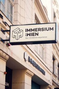 Außenschild des Immersium Wien mit geometrischem Würfel-Logo an der Gebäudefassade.