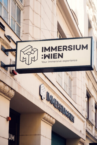 Außenschild des Immersium Wien mit geometrischem Würfel-Logo an der Gebäudefassade.