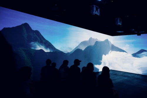 Besucher betrachten eine Berglandschaft, die über die Wände des 360-Grad-Showrooms projiziert wird.