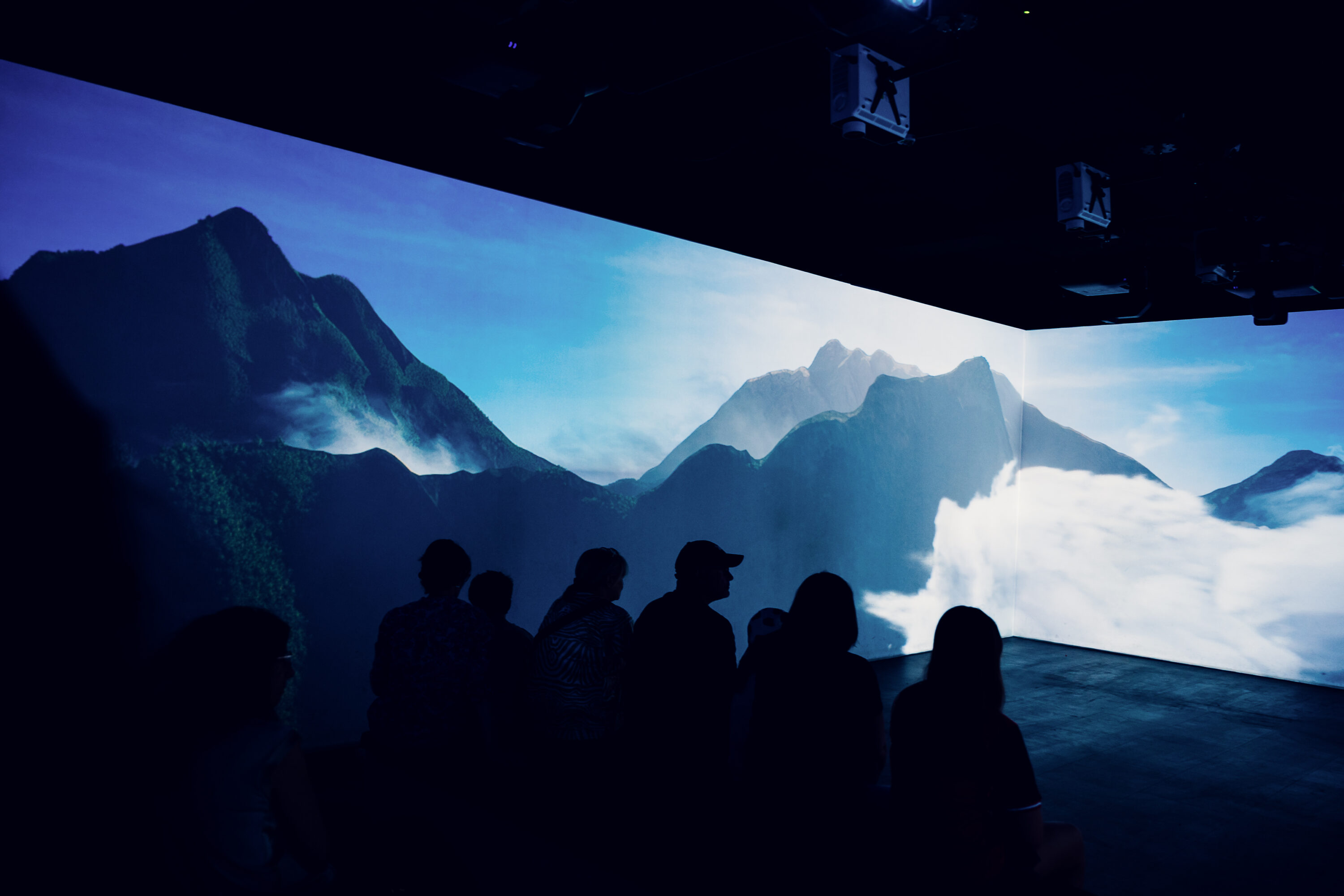 Besucher betrachten eine Berglandschaft, die über die Wände des 360-Grad-Showrooms projiziert wird.