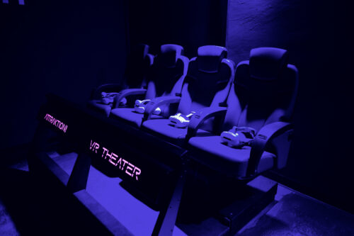 Reihe von Bewegungssitzen mit Gurten im VR-Theater, beleuchtet von violettem Licht.