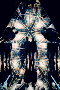 Silhouette von Adriana und Mario im verspiegelten Pyramidenraum, umgeben von goldenen geometrischen Lichtmustern.