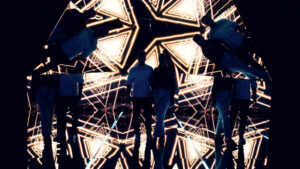 Two visitors standing in the pyramid room with geometric golden projections reflected around them.