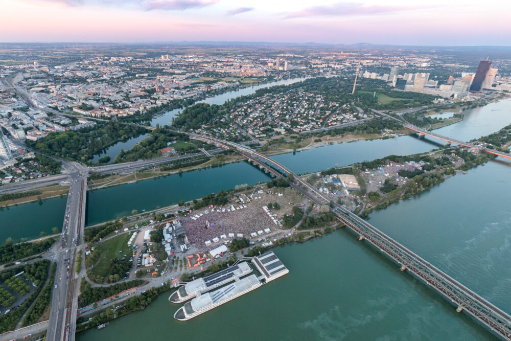 Aerial view of Donauinselfest on the Donauinsel at dusk, the festival ground between the Danube and the Neue Donau with Vienna's skyline behind